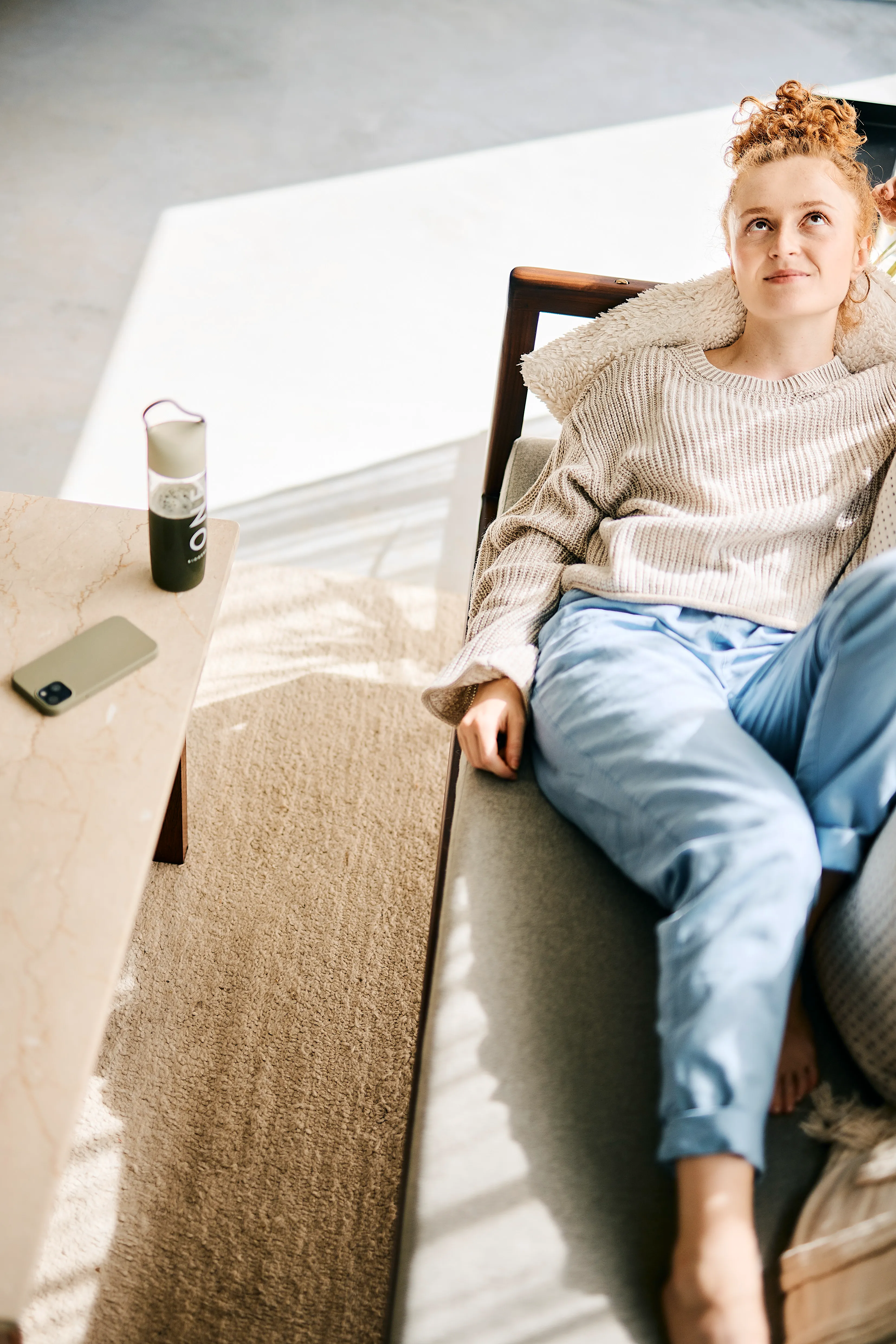 Eine entspannte Frau auf dem Sofa mit der BIOGENA ONE Trinkflasche auf dem Couchtisch zur Vorbereitung der täglichen Nährstoff-Routine