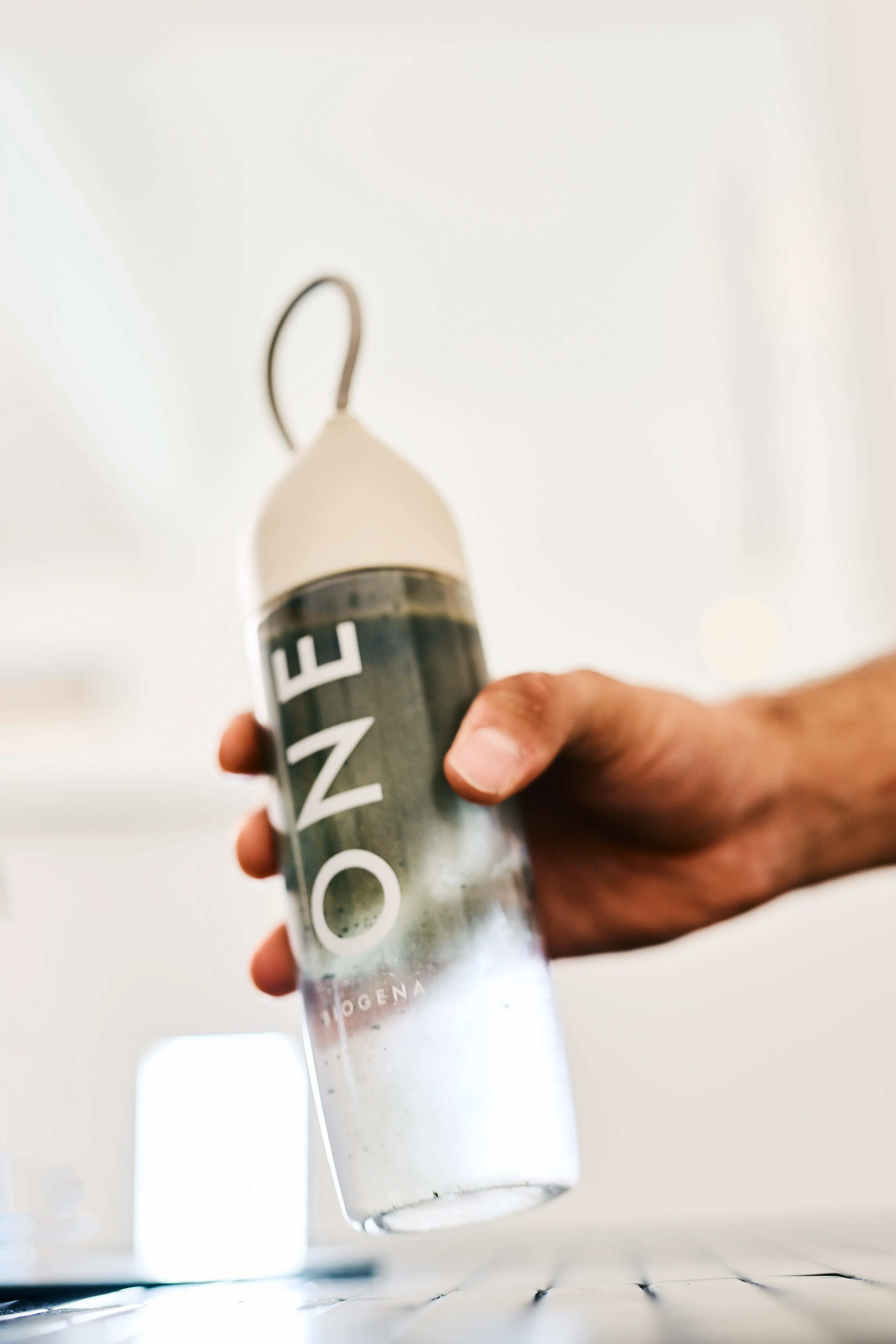 Nahaufnahme einer Hand, die die einsatzbereite BIOGENA ONE Flasche mit dem frisch zubereiteten grünen All-in-One Drink hält
